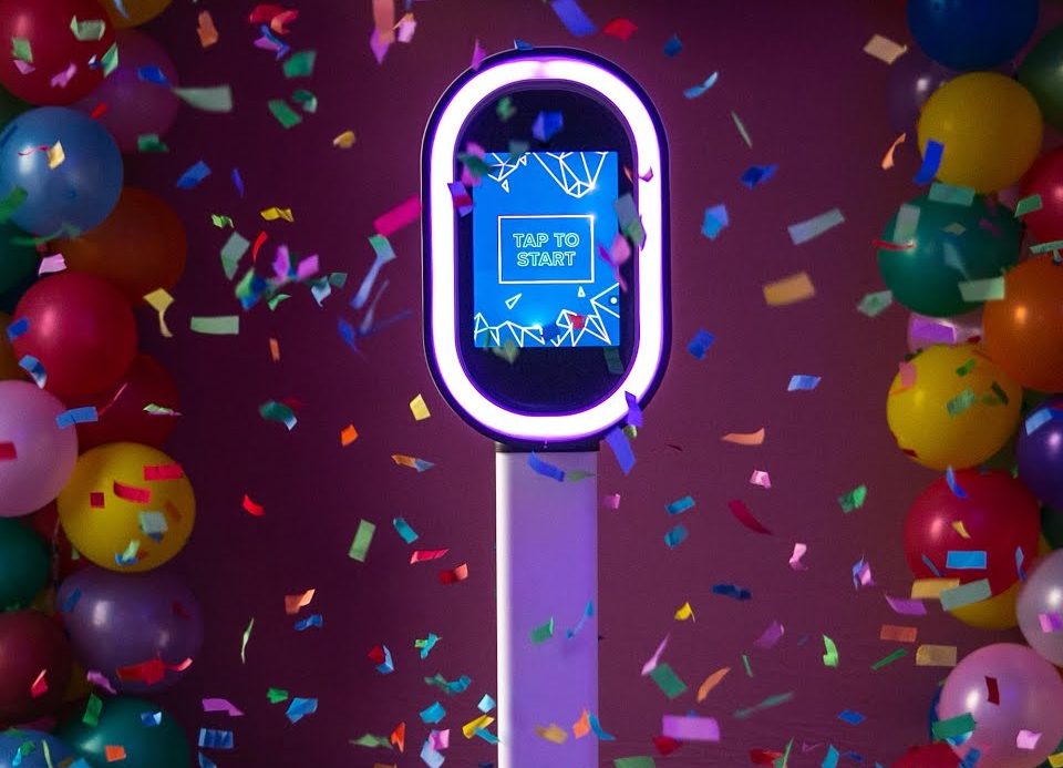 Een feestelijke fotomoment met een touchscreen en ballonnen in een kleurrijke setting.